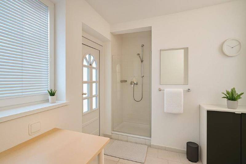 Helles Badezimmer mit Duschkabine, Fenster und schlichtem, modernem Design mit weißen Fliesen.