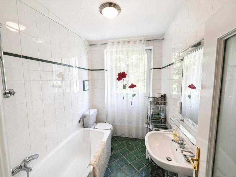 Helles Badezimmer mit weiß gefliesten Wänden, grünen Bodenfliesen und Badewanne.