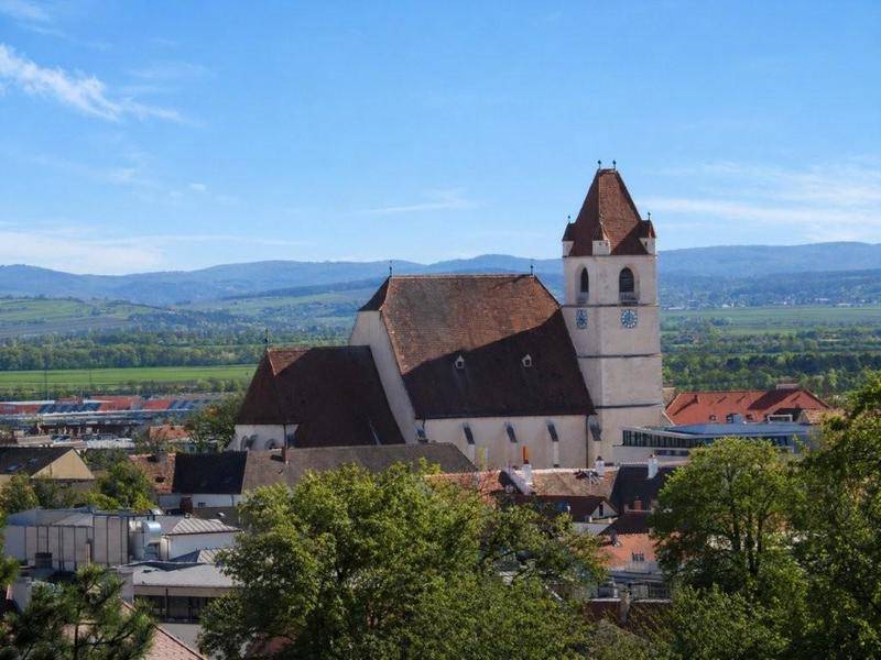 Panoramablick auf eine Stadt mit einer historischen Kirche und umliegenden Bergen.