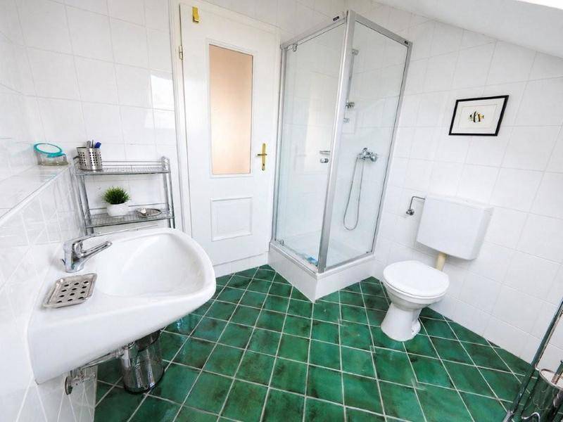 Badezimmer mit Duschkabine, Waschbecken und WC, ausgestattet mit weißen und grünen Fliesen.