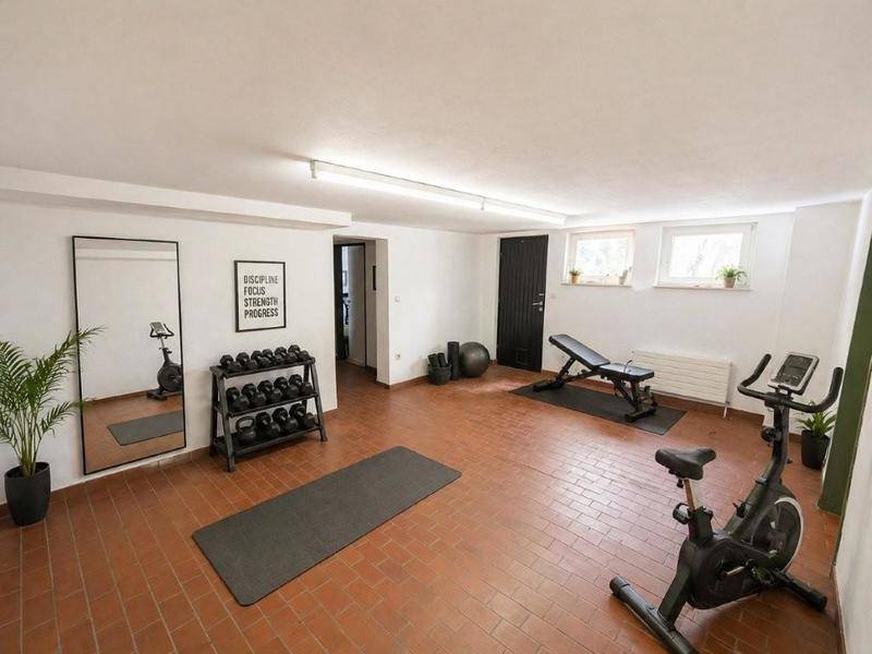 Geräumiger Fitnessraum mit verschiedenen Trainingsgeräten, Spiegel und Fliesenboden.