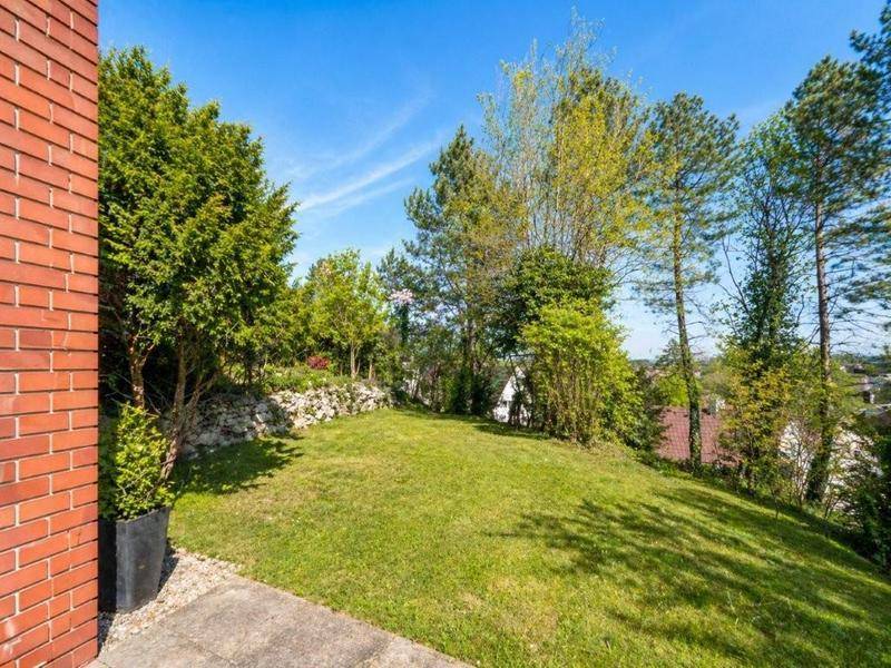 Gepflegter Gartenbereich mit Rasenfläche, Bäumen und einer Natursteinmauer.
