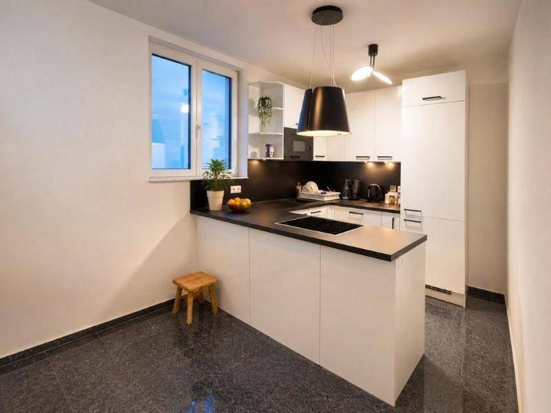 Moderne Einbauküche mit weiß-glänzenden Fronten, dunkler Arbeitsplatte und integriertem Kochfeld.