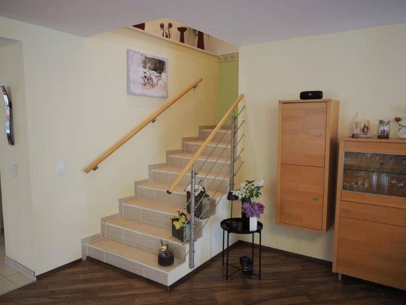 Helle Treppe mit Holzgeländer und modernen Edelstahlstäben.