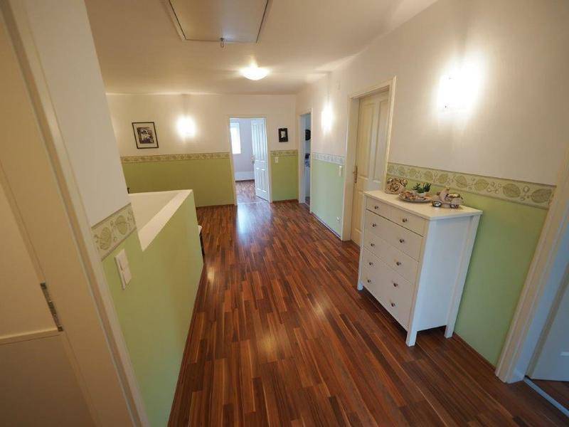 Langer Flur mit Holzboden, hellgrünen Wänden und weißer Kommode.