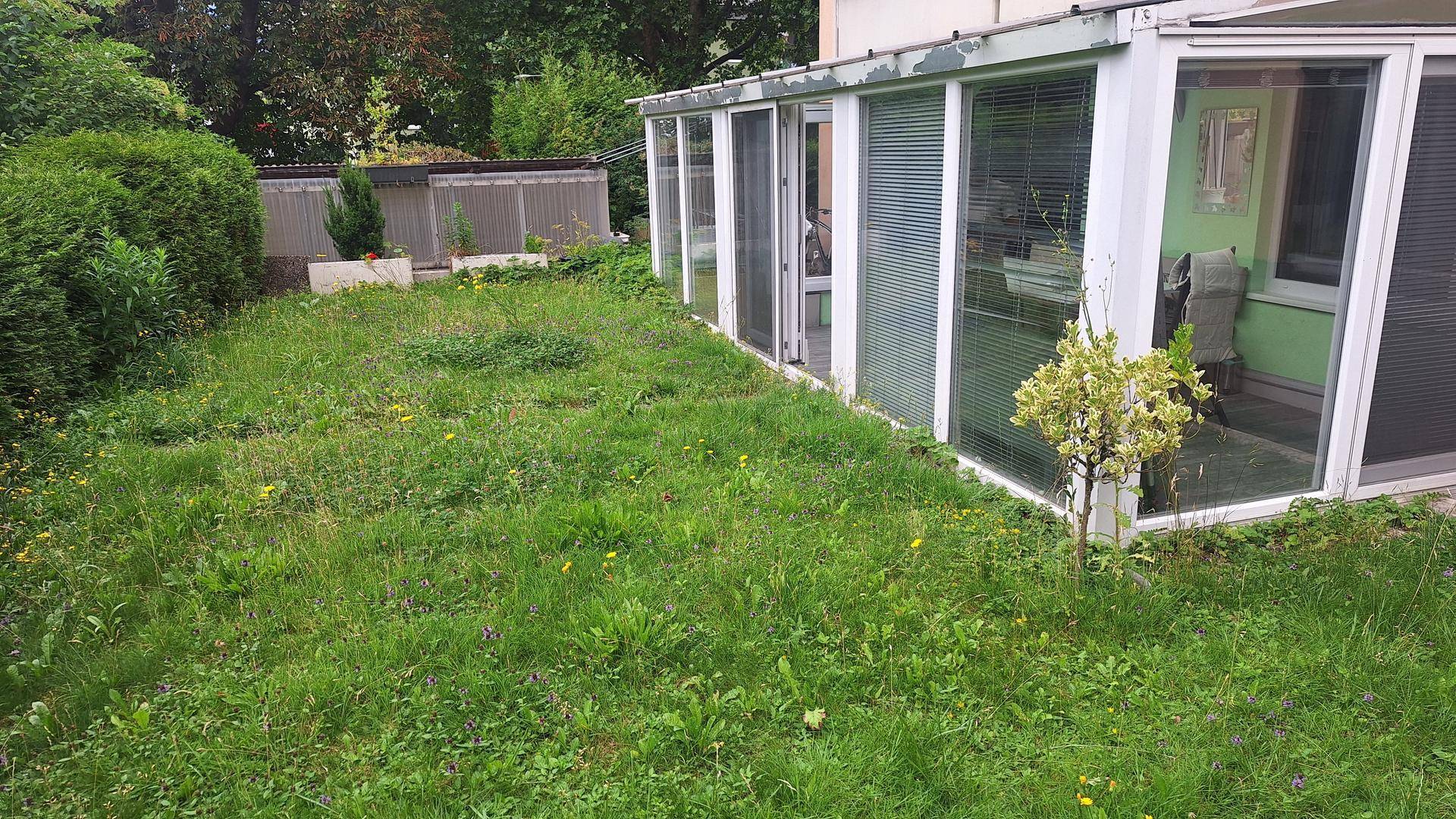 Grüner Gartenbereich neben dem Gebäude mit Wintergarten, bietet Platz für Erholung im Freien.