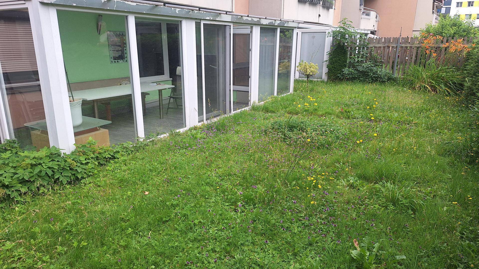 Weitläufiger Garten mit Rasenfläche und angrenzendem Wintergarten, umgeben von Hecken.