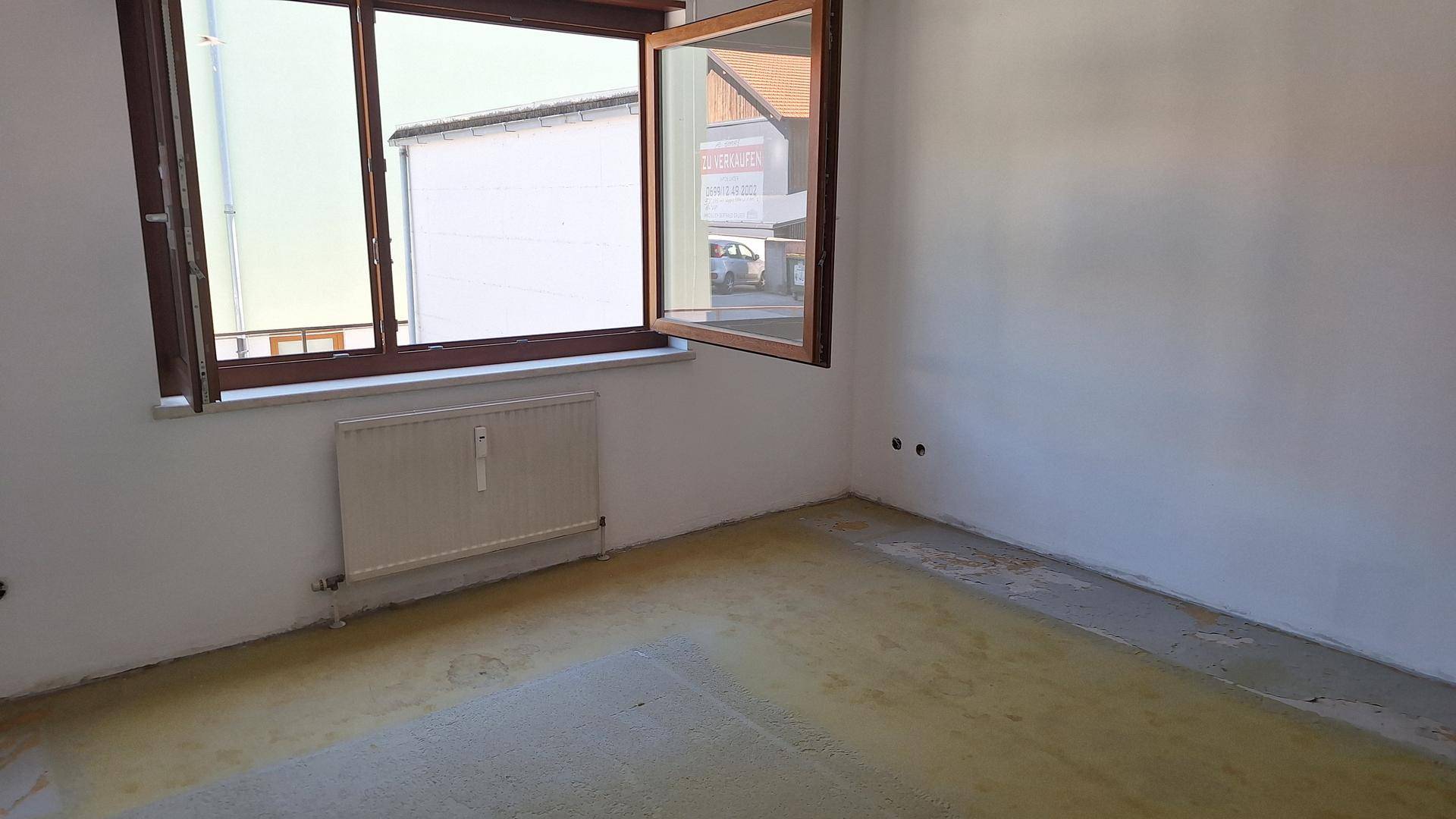 Unmöblierter Raum mit Fenster, Heizkörper und Blick auf die Straße und angrenzende Gebäude.