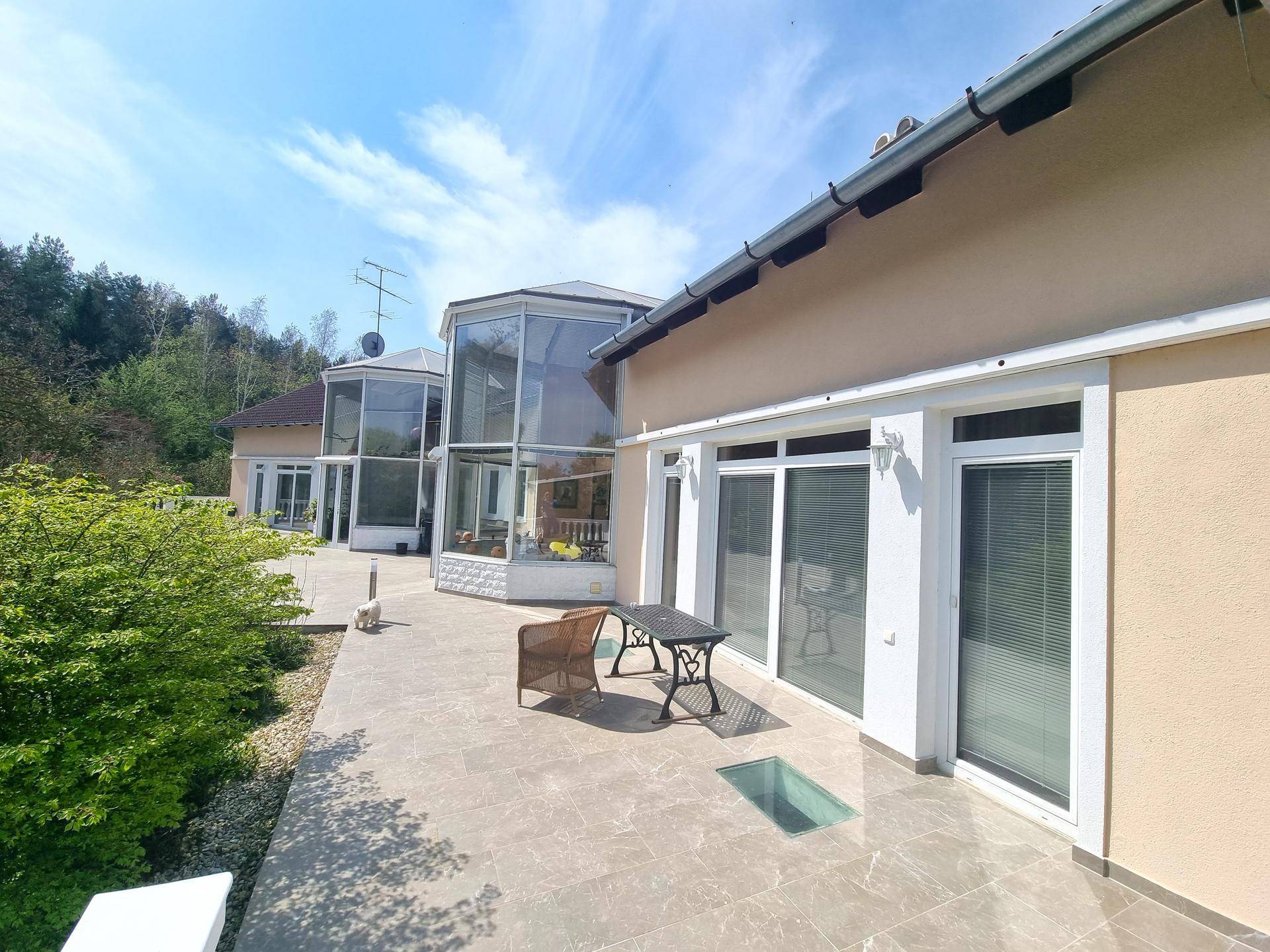 Seitliche Terrasse mit Fliesenboden und Blick auf die verglasten Anbauten des Hauses.