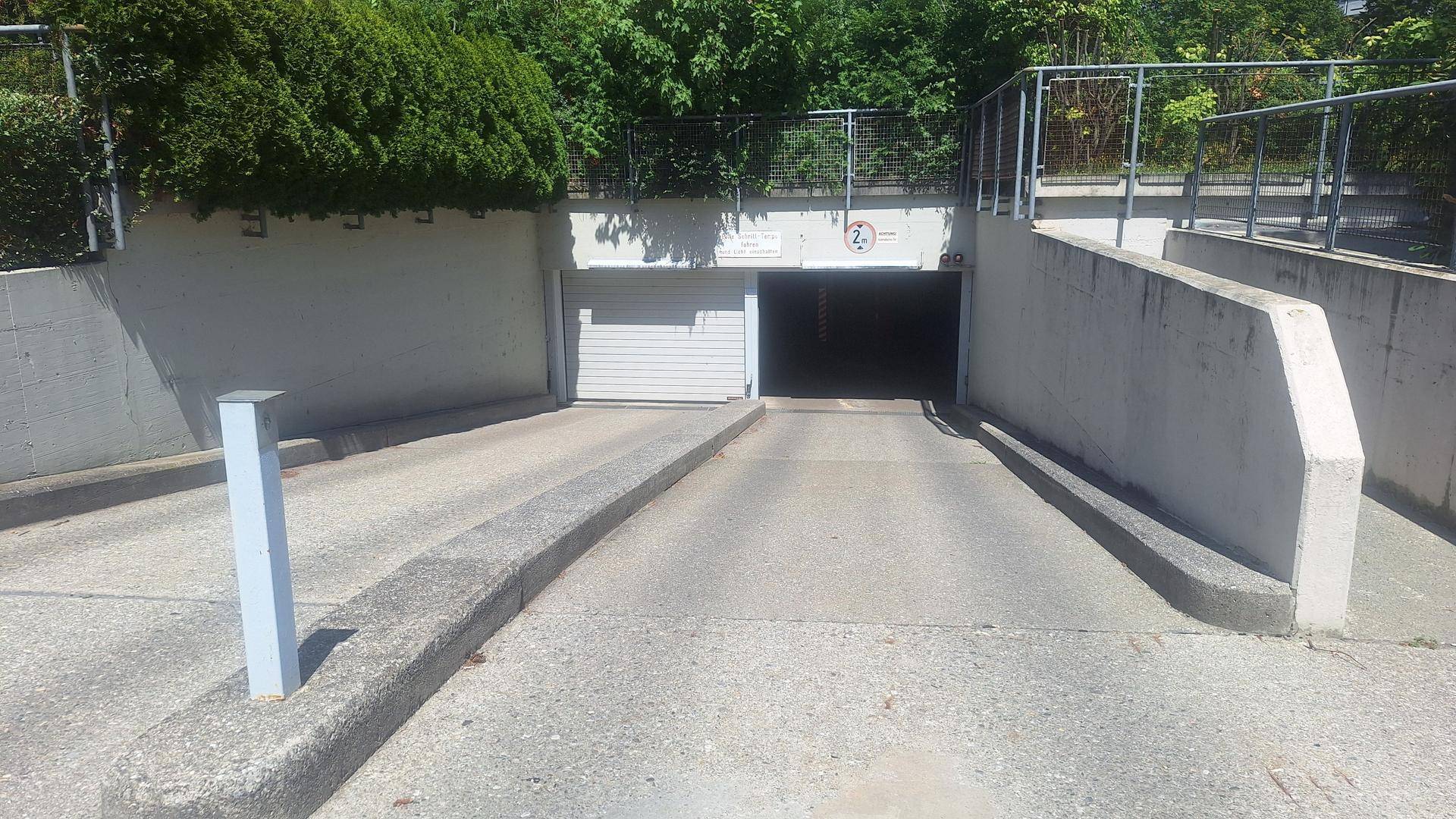 Zufahrt zu einer Tiefgarage mit Betonwänden und Rolltor, bietet sichere Parkmöglichkeiten.