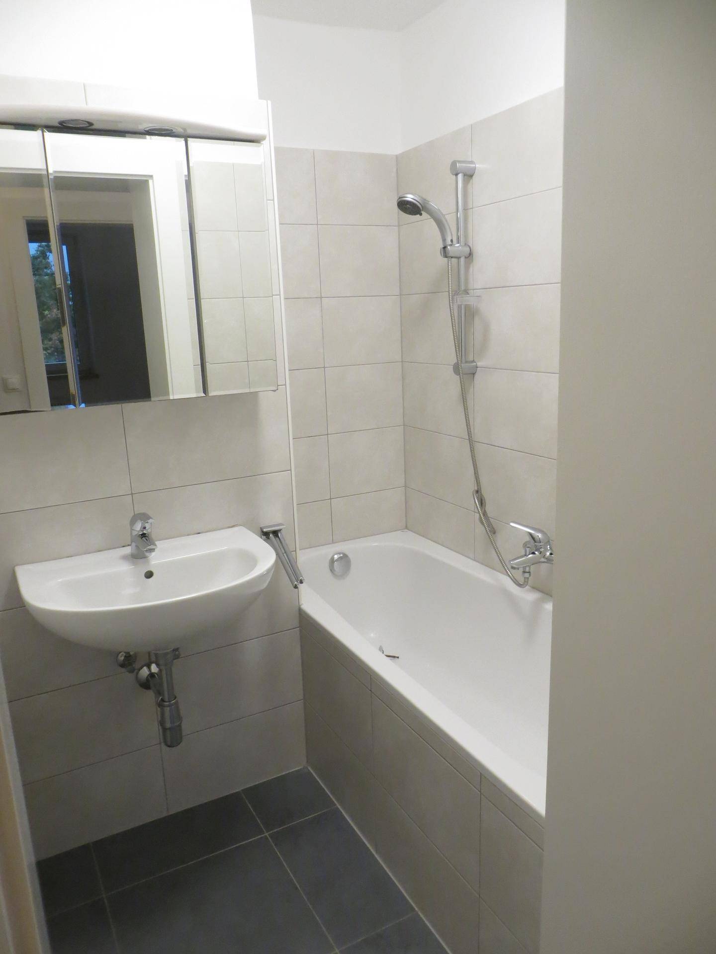 Modernes Badezimmer mit Badewanne, Dusche und hellen Fliesen, ausgestattet mit einem Spiegelschrank.