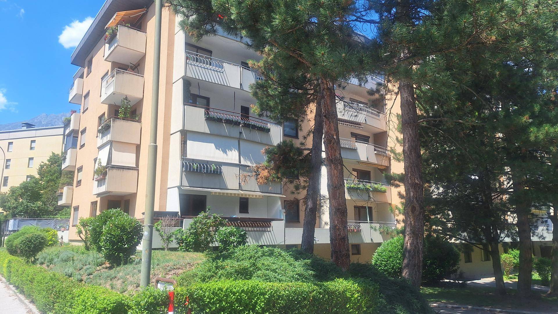 Mehrfamilienhaus mit Balkonen, umgeben von Bäumen und gepflegter Grünanlage.