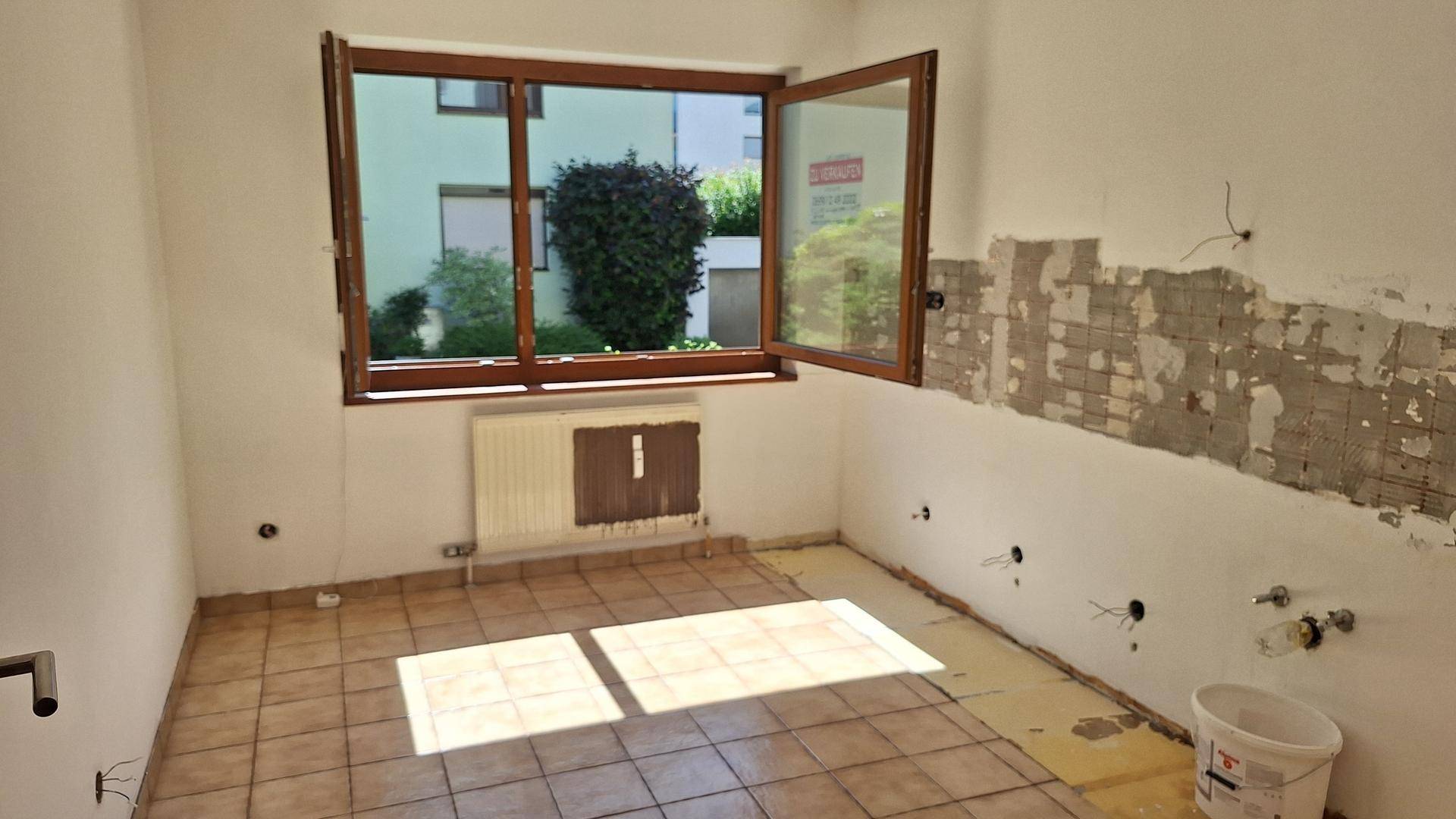 Renovierungsbedürftige Küche mit Fliesenboden, Heizkörper und vorbereiteten Anschlüssen.