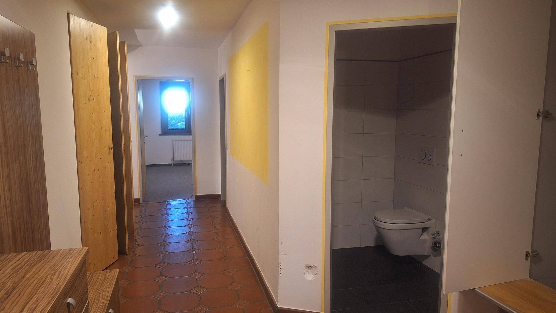 Heller Flur mit Terrakotta-Fliesenboden und Zugang zu einem Gäste-WC und weiteren Räumen.