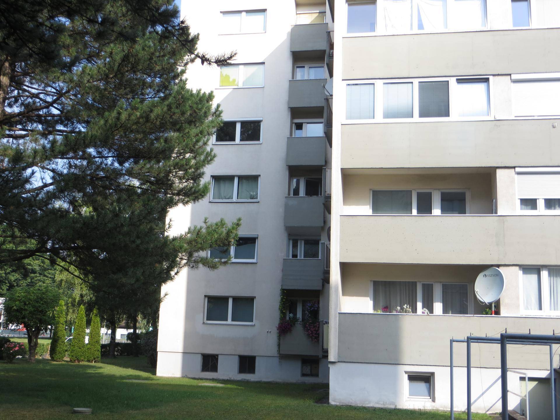 Ansicht eines Mehrfamilienhauses mit Balkonen und grüner Umgebung an einem sonnigen Tag.