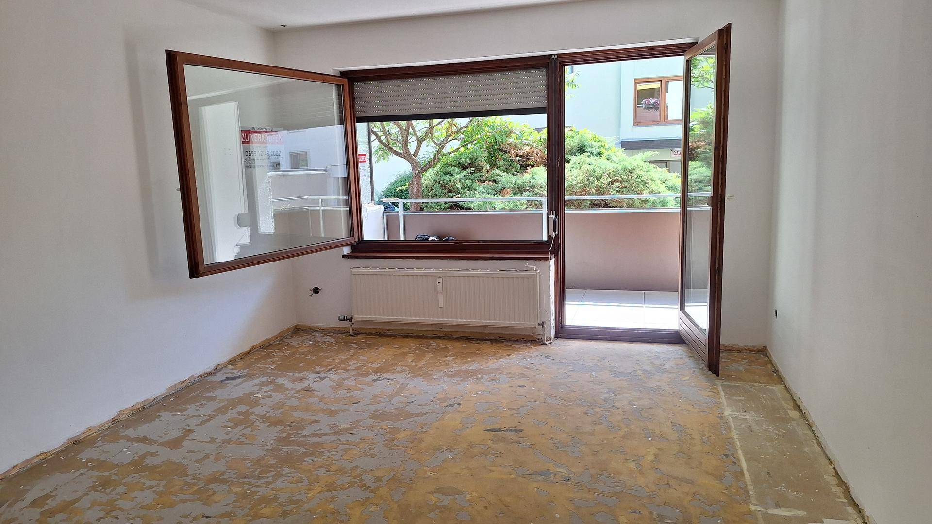 Helles Zimmer mit Blick ins Grüne, Heizkörper und Zugang zu einem kleinen Balkon.