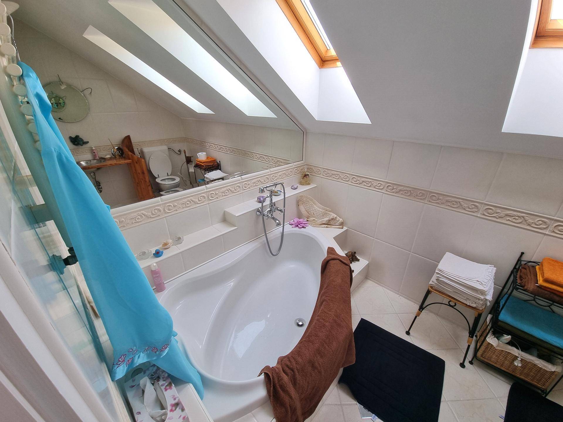 Helles Badezimmer im Dachgeschoss mit Eckbadewanne, Dachfenster und großem Spiegel.