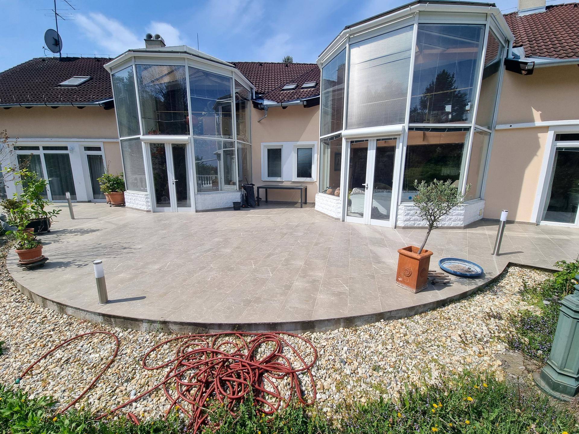 Geräumige Terrasse mit Fliesenboden und Zugang zu den verglasten Wintergärten des Hauses.