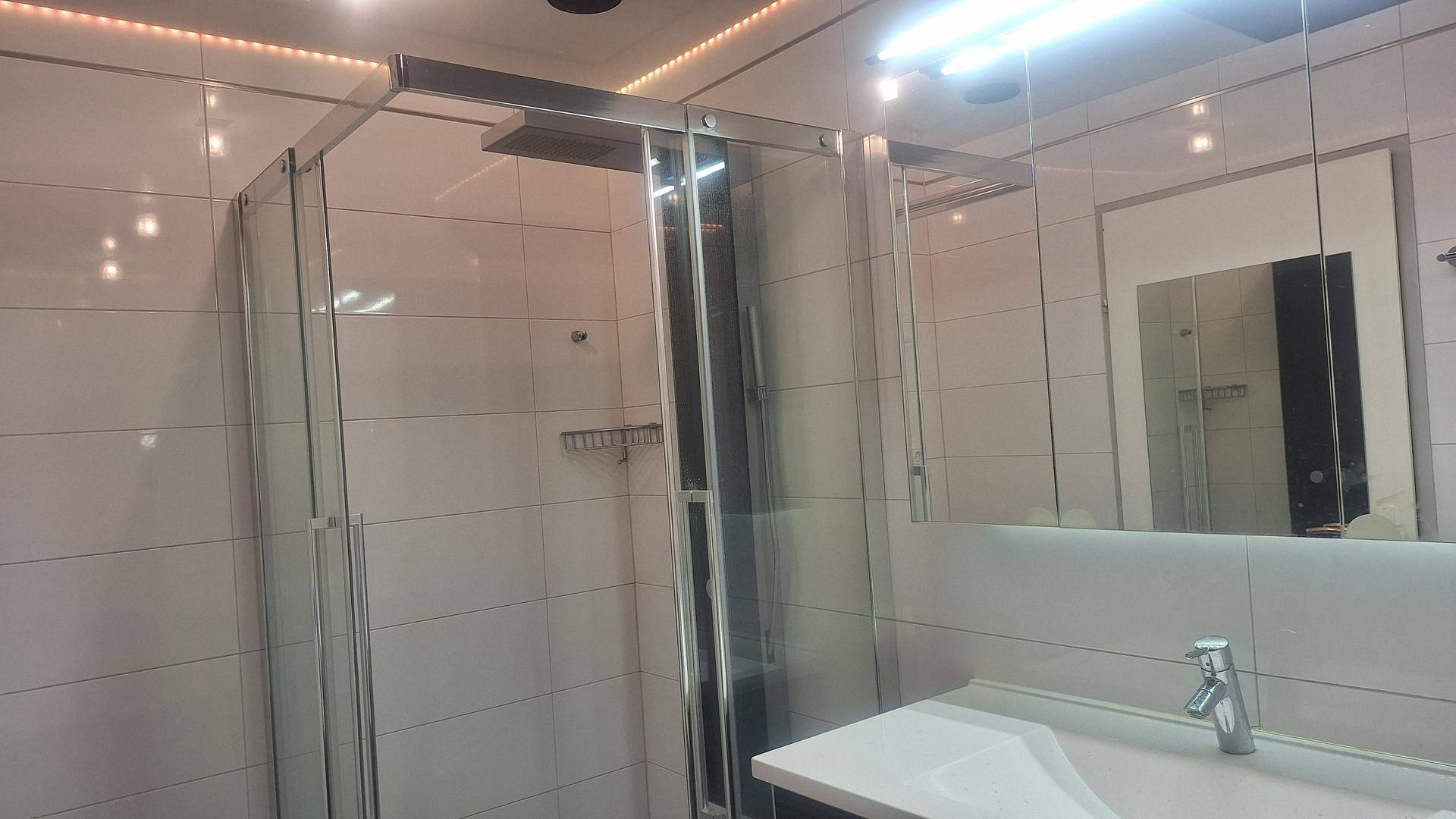 Helles Badezimmer mit moderner Duschkabine aus Glas, Waschtisch und Spiegelschrank, weiß gefliest.