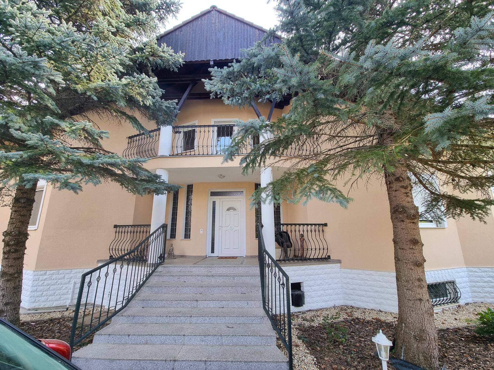 Repräsentative Hausfassade mit breiter Treppe, Balkonen und dekorativen Bäumen im Vorgarten.