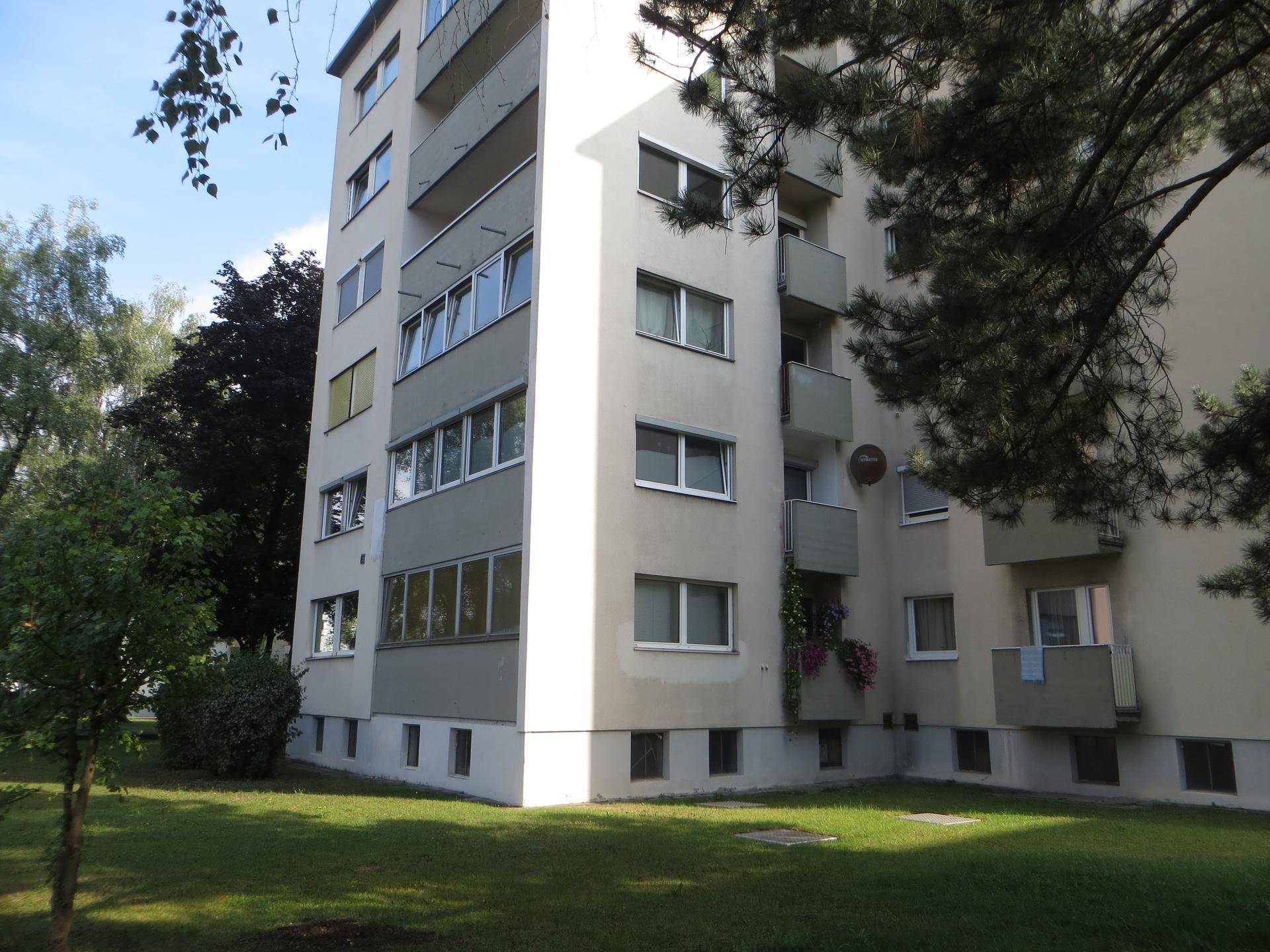 Mehrfamilienhaus mit gepflegter Grünfläche und Bäumen, umgeben von einer ruhigen Wohngegend.