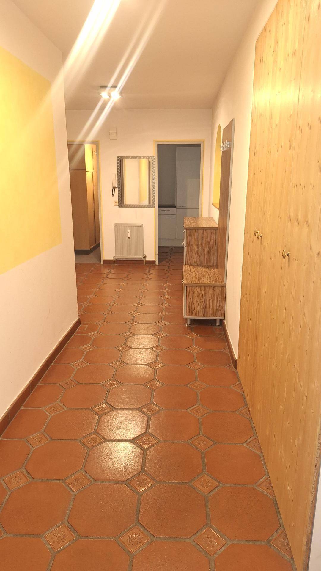 Langer Flur mit gemusterten Terrakotta-Fliesen und Holzmöbeln, der zu weiteren Räumen führt.