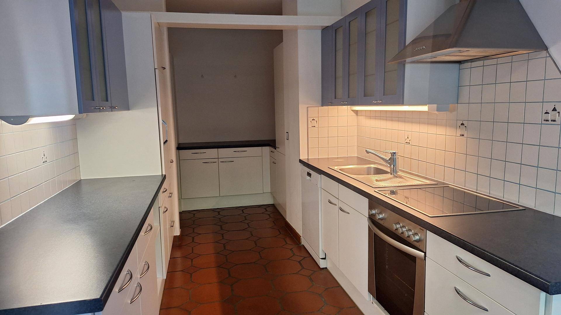 Funktionale Küche mit blaugrauen Oberschränken, dunklen Arbeitsplatten und Terrakotta-Fliesenboden.