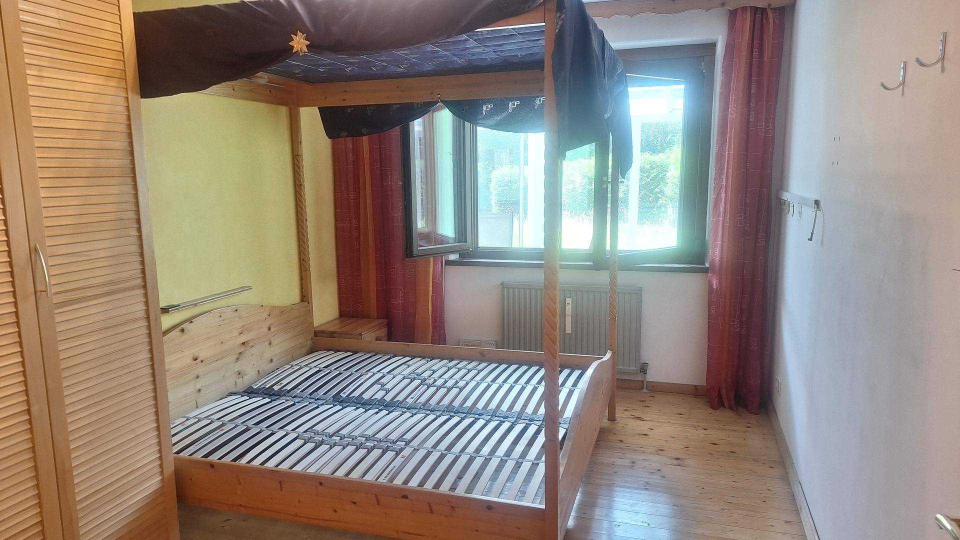 Gemütliches Schlafzimmer mit Himmelbett aus Holz, Holzboden und Fenster mit Blick ins Grüne.