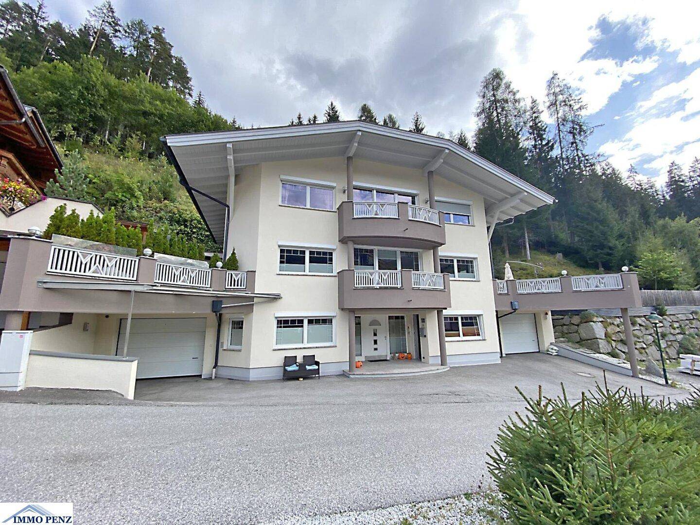 Mehrstöckiges Haus mit Balkonen und Garagen, eingebettet in eine grüne Hanglandschaft.