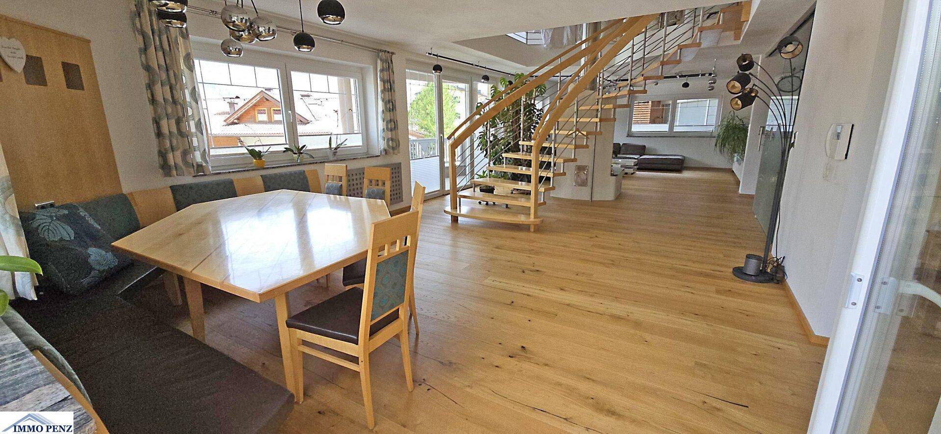 Heller Essbereich mit Holztisch, Eckbank und einer eleganten Wendeltreppe im Hintergrund.
