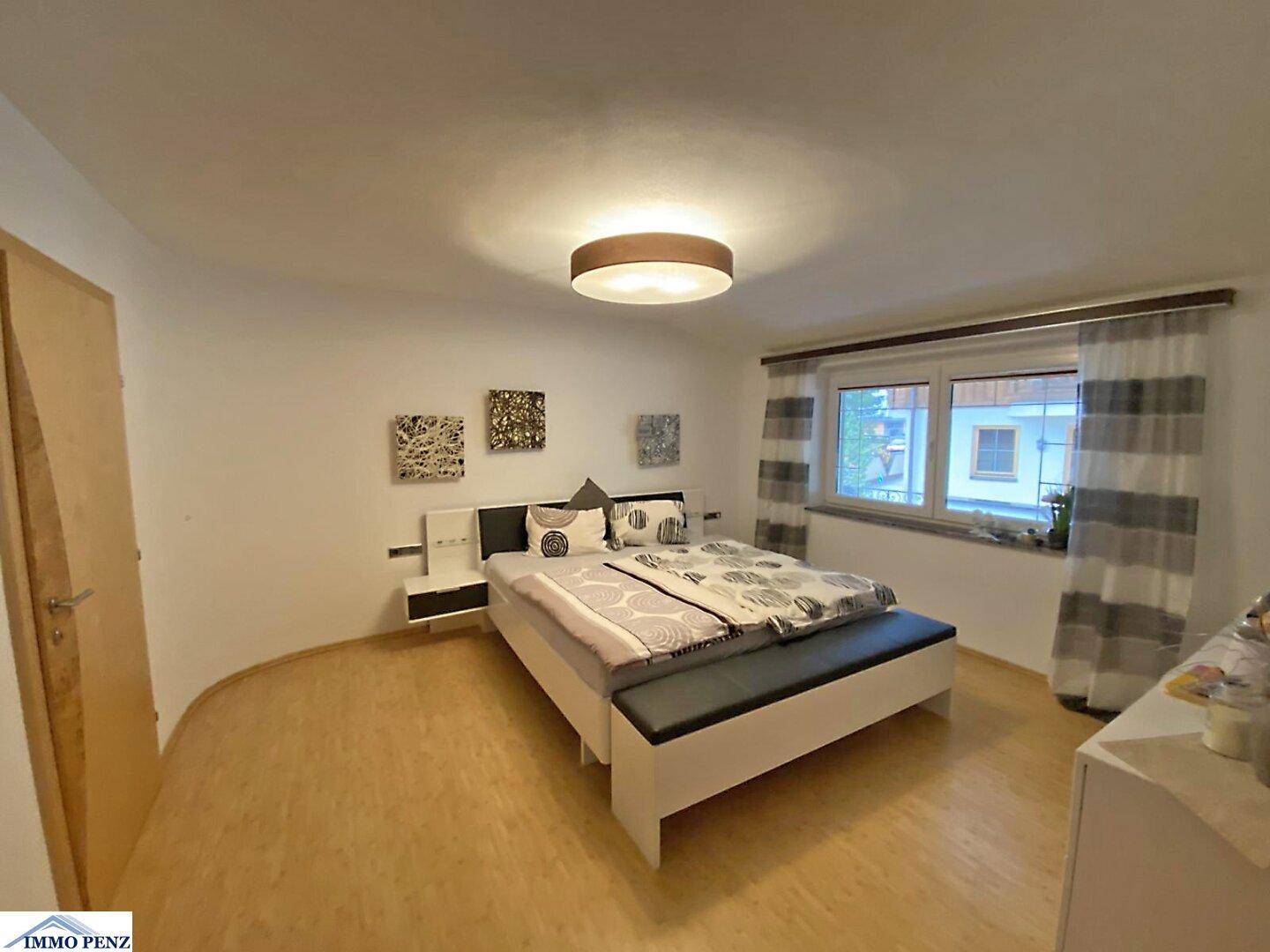Gemütliches Schlafzimmer mit Doppelbett, Nachttischen und einem Fenster mit gestreiften Vorhängen.