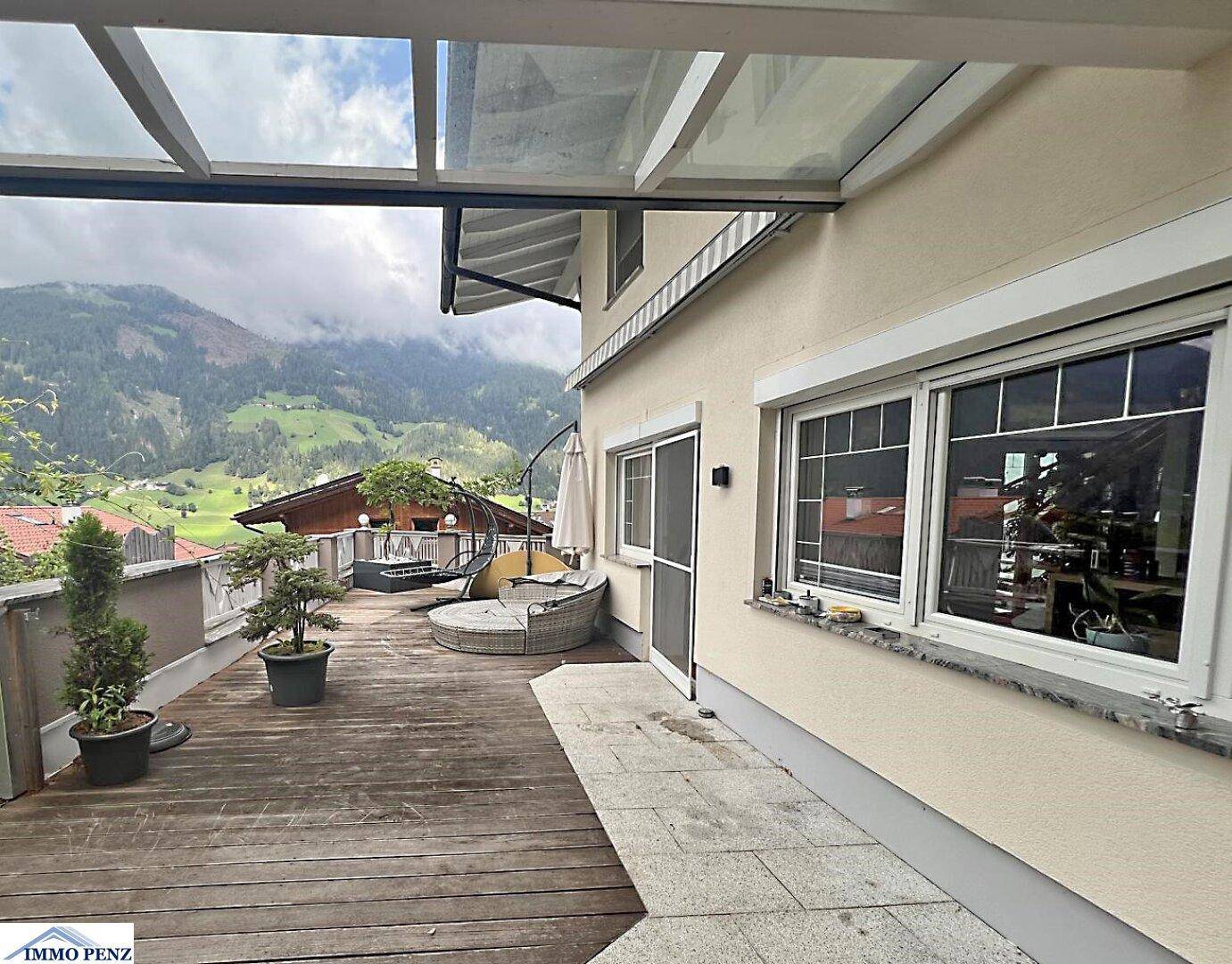 Große Holzterrasse mit Glasdach, Outdoor-Möbeln und beeindruckendem Bergblick.