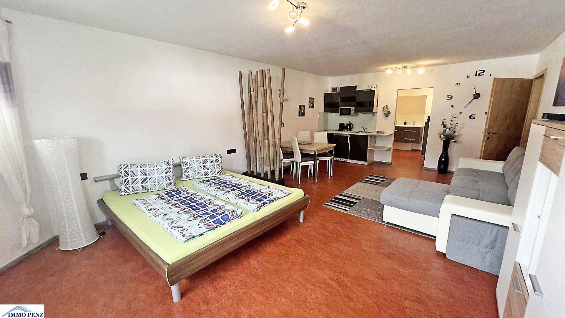 Offener Wohnbereich mit Schlafgelegenheit, Sofa, Essbereich und integrierter Küchenzeile in modernem Stil.