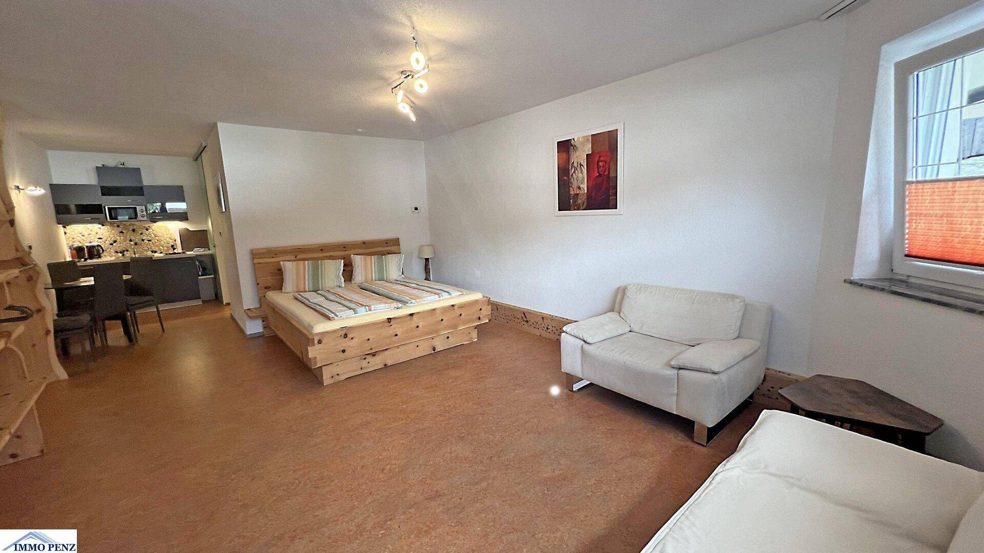 Offener Wohnbereich mit Bett, Sofa und einer kleinen Küchenzeile im Hintergrund.