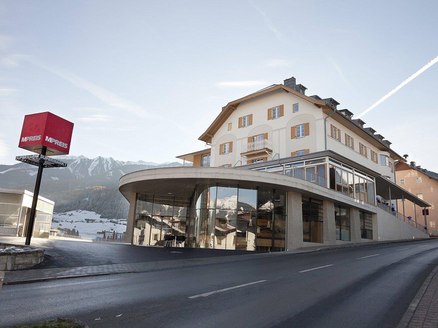 Das moderne Gebäude mit Supermarkt im Erdgeschoss und Wohnungen darüber, eingebettet in die Berglandschaft.