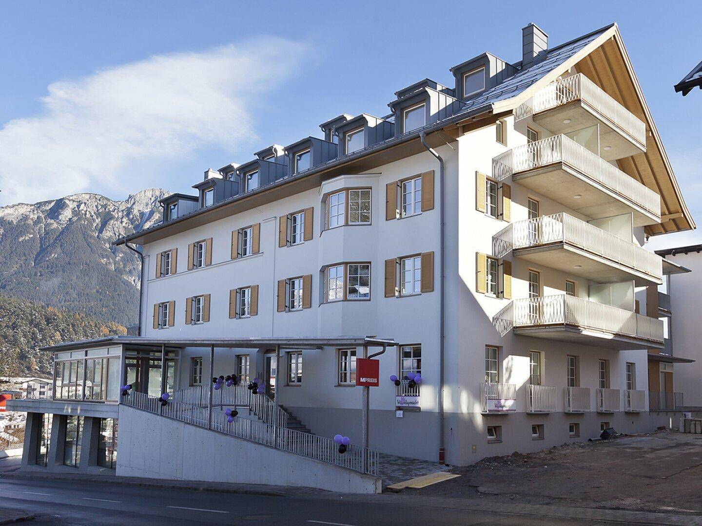 Ansicht des Gebäudes mit mehreren Balkonen, Mansarddach und beeindruckendem Bergpanorama.