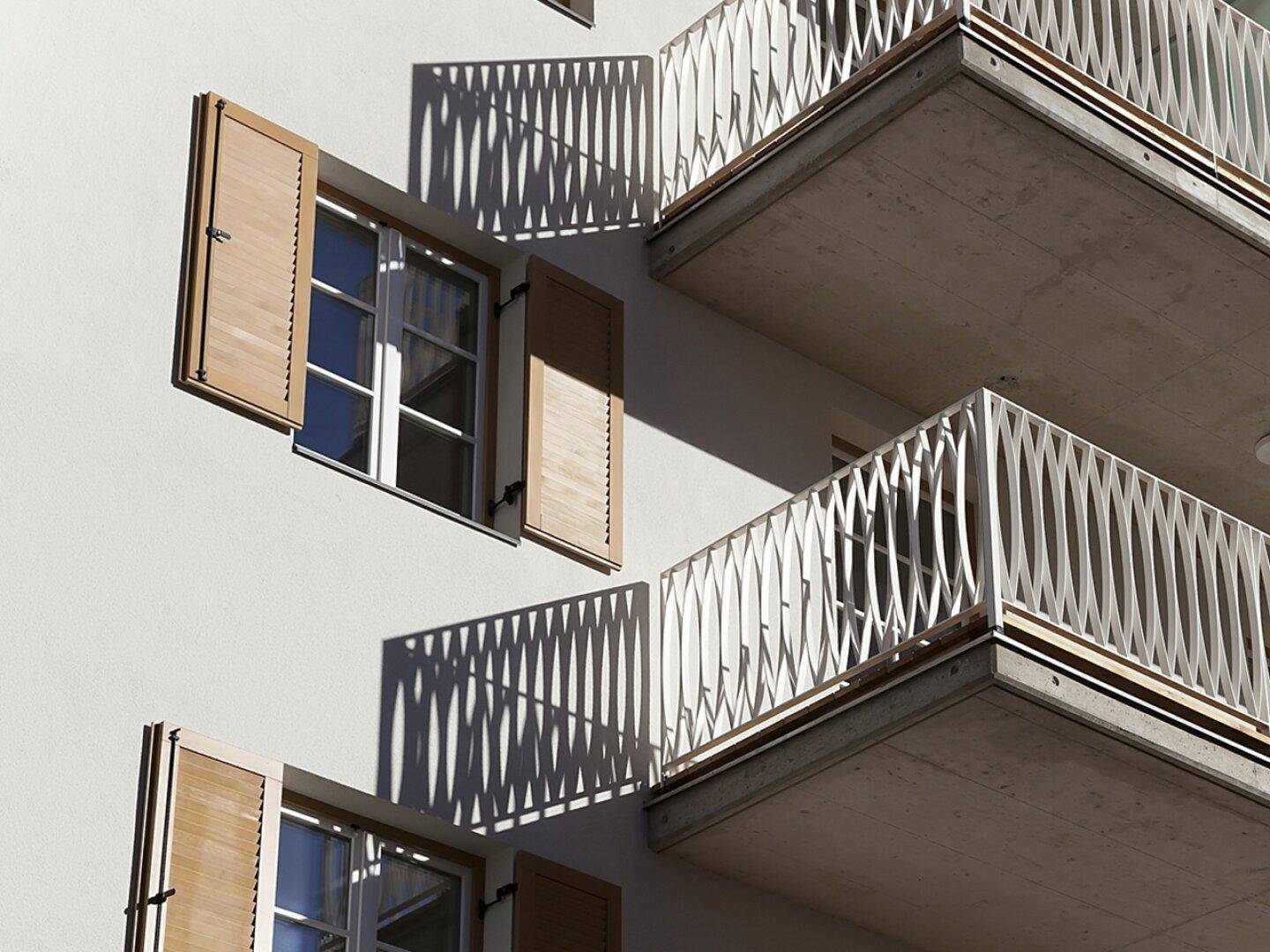 Detailansicht der Fassade mit Holzfensterläden und Balkonen mit dekorativen Geländern.