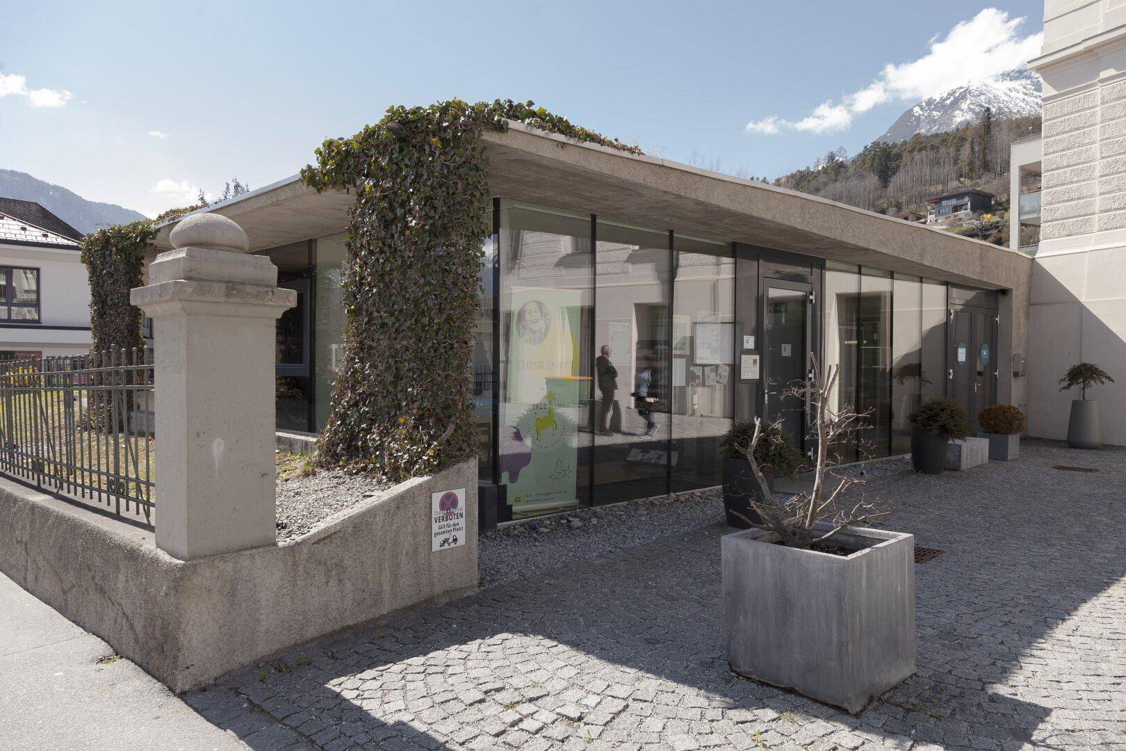 Moderne Glasfassade eines Anbaus mit begrüntem Dach und gepflastertem Vorplatz.