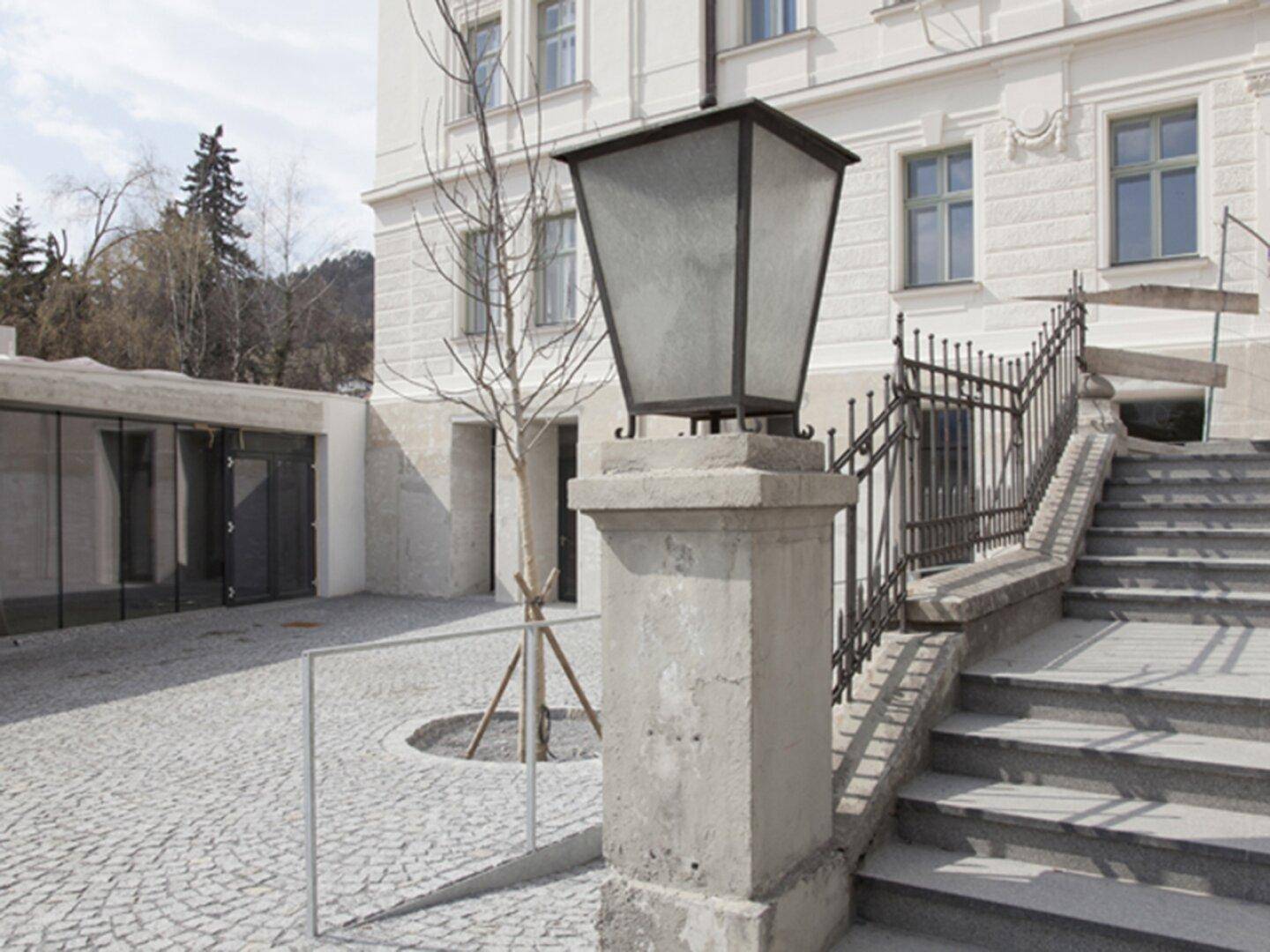 Historische Steintreppe mit schmiedeeisernem Geländer und klassischer Laterne am Eingang.