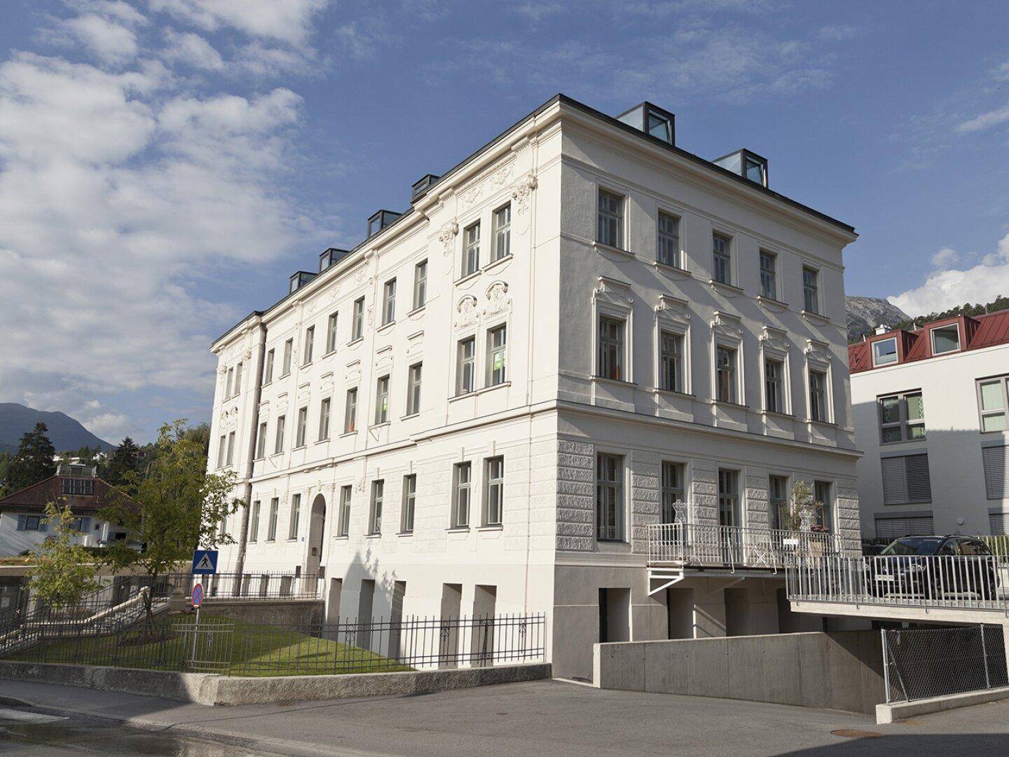 Historisches Gebäude mit klassischer Architektur, großen Fenstern und einem Eingang zu einer Tiefgarage.