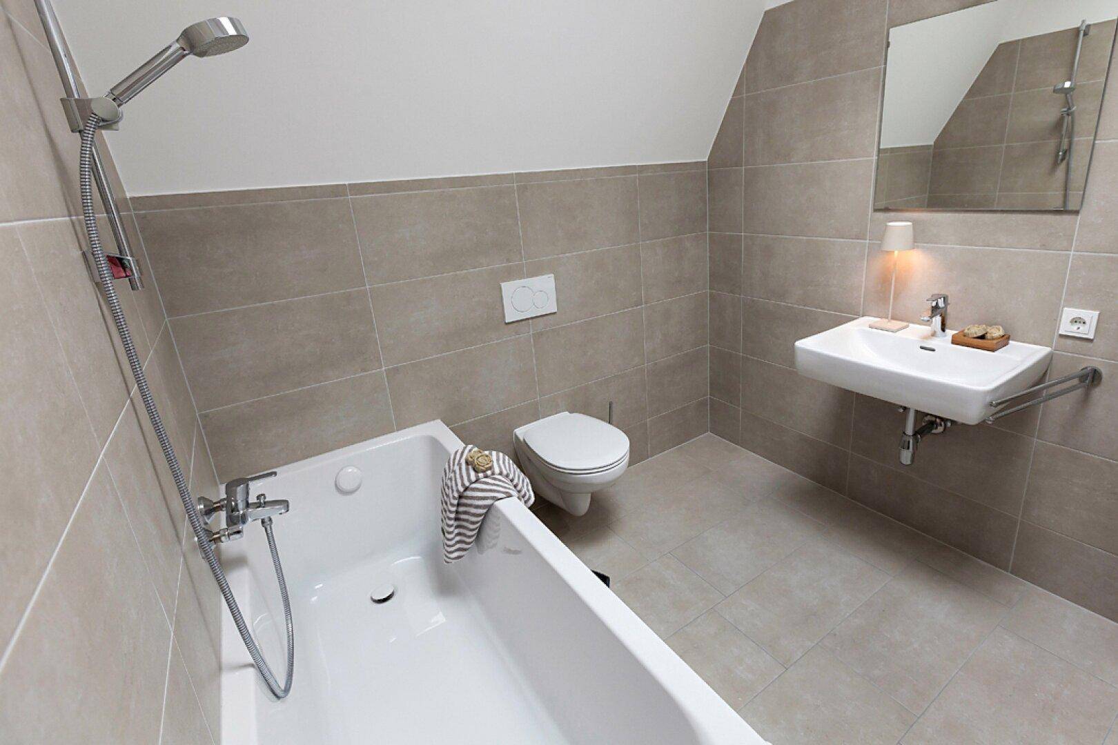 Modernes Badezimmer mit Badewanne, WC und Waschbecken unter einer Dachschräge.