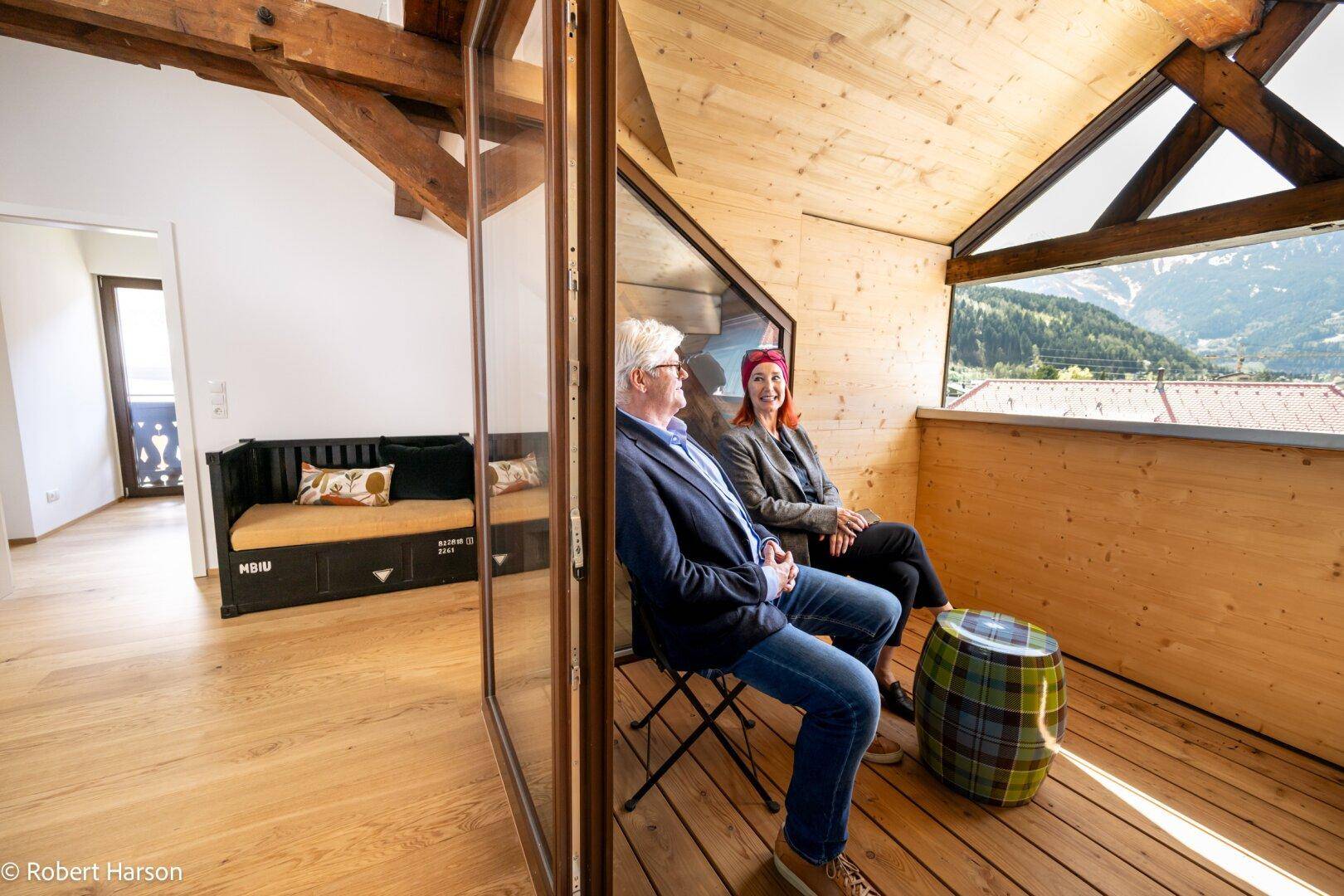 Verglaster Wohnbereich mit Holzwänden, Bergblick und Sitzgelegenheiten.
