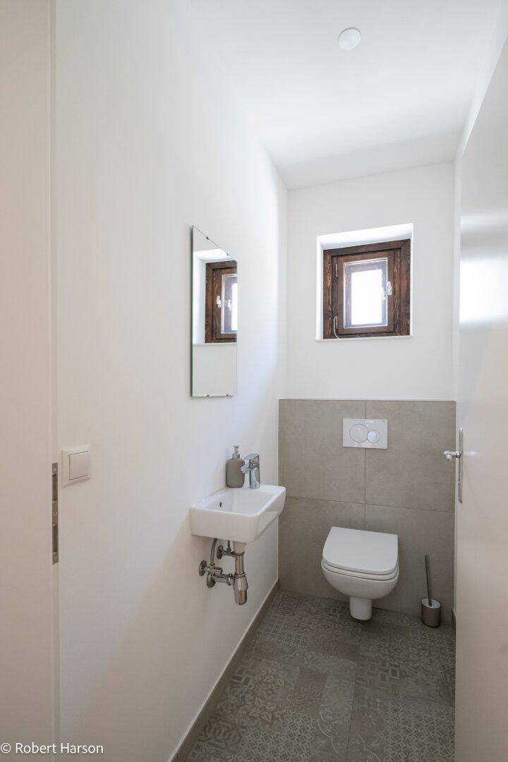 Kleines Gäste-WC mit Wand-WC, Waschbecken und Fenster.