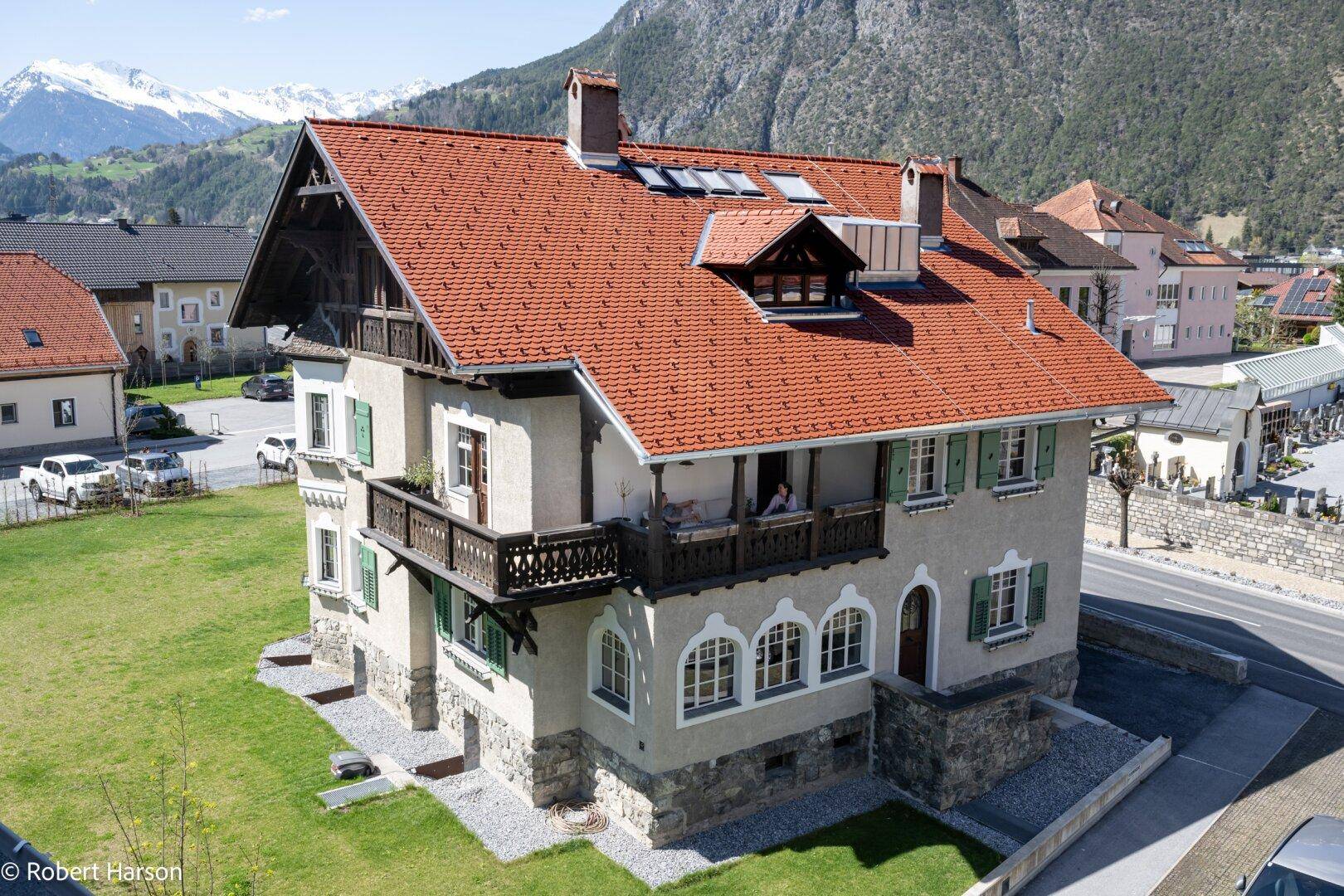 Traditionelles Gebäude mit rotem Ziegeldach, Holzbalkonen und Bergblick.