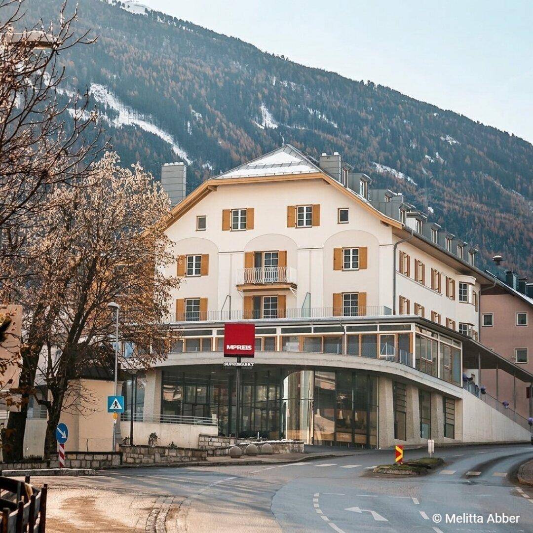 Gebäude mit moderner Glasfront und traditionellen Elementen, eingebettet in eine alpine Landschaft.