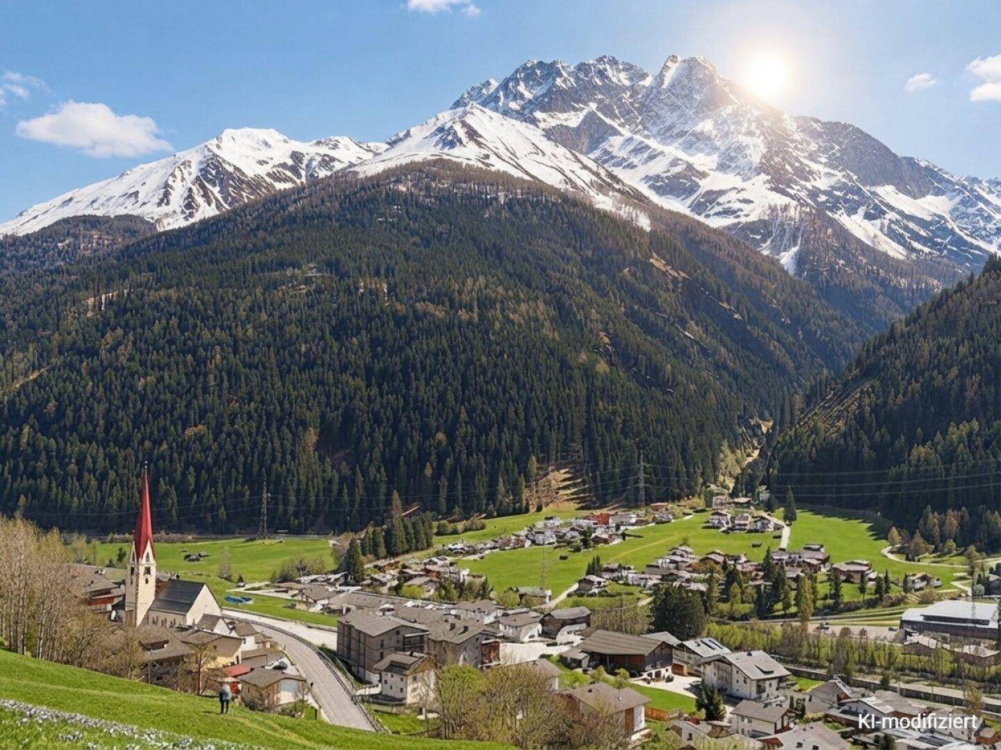 Panoramablick auf ein malerisches Dorf in einem Tal mit schneebedeckten Bergen und strahlendem Sonnenschein.