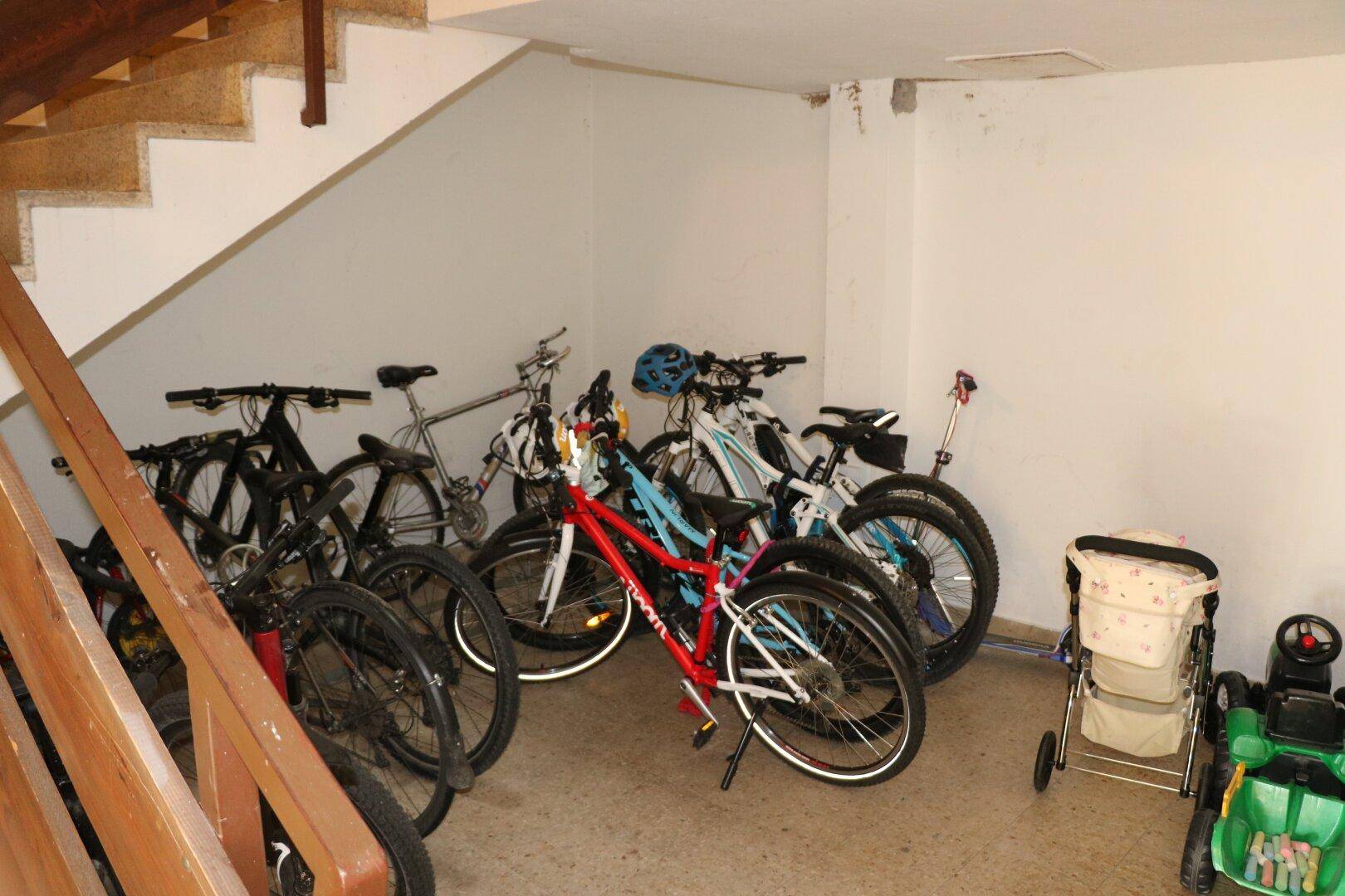 Fahrradabstellraum unter einer Treppe mit mehreren Fahrrädern und Kinderwagen.