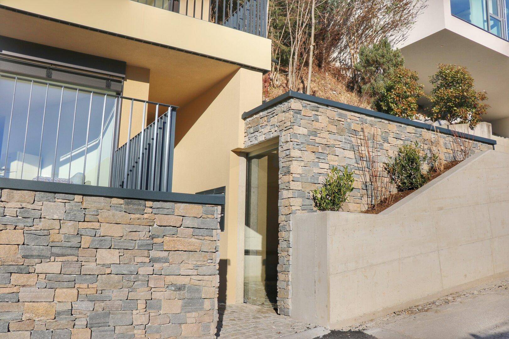 Detailansicht der modernen Fassade mit Natursteinverkleidung und Betonstrukturen am Hang.