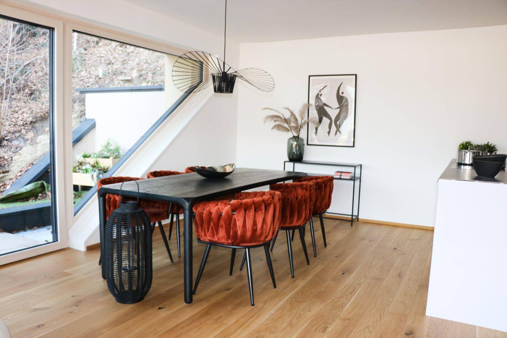 Eleganter Essbereich mit großem schwarzen Tisch, orangefarbenen Stühlen und Blick ins Grüne.