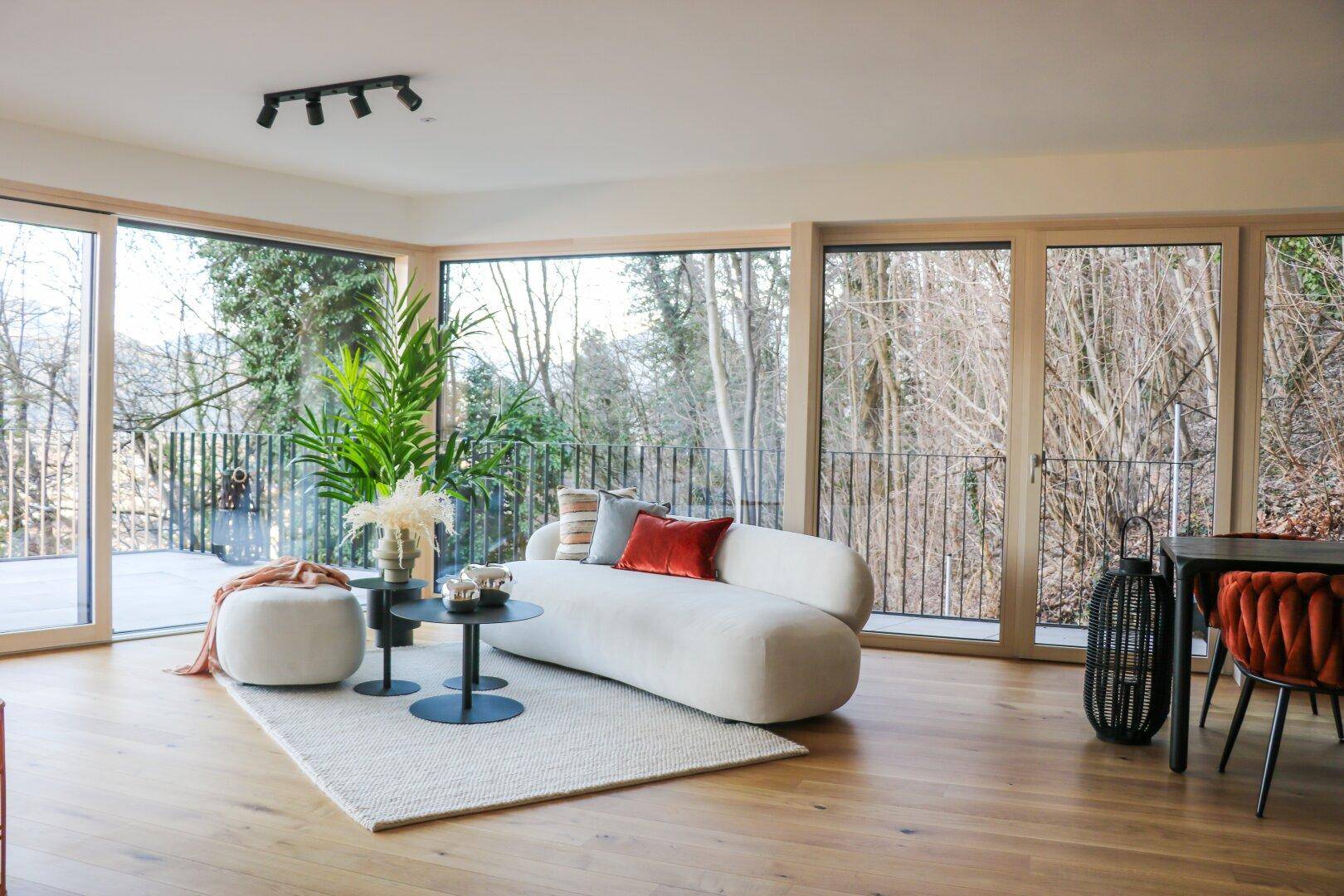 Geräumiges Wohnzimmer mit bequemer Couch, Holzboden und Panoramafenstern zur Natur.